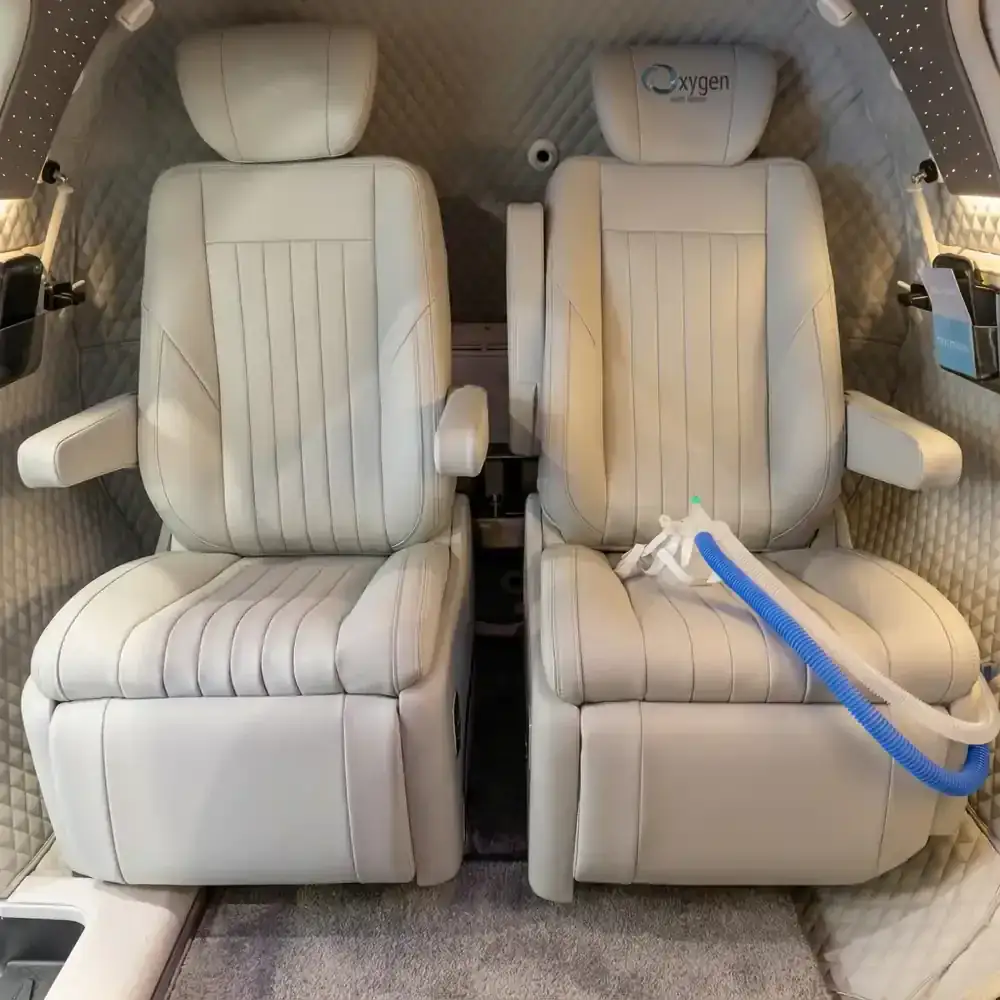 Two cream quilted leather captain's chairs inside the M5500 cabin with diamond-stitched wall lining, an Oxygen Health Systems embroidered headrest, and a blue oxygen mask hose